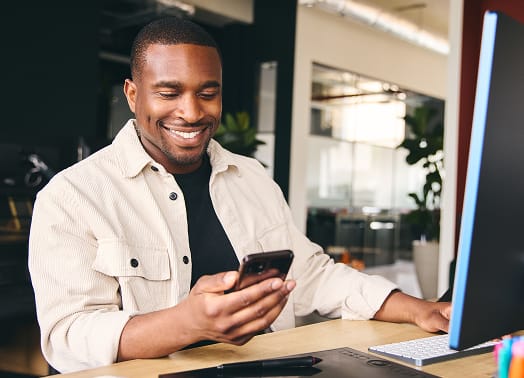 Man sitting at desk smiling and looking at cell phone